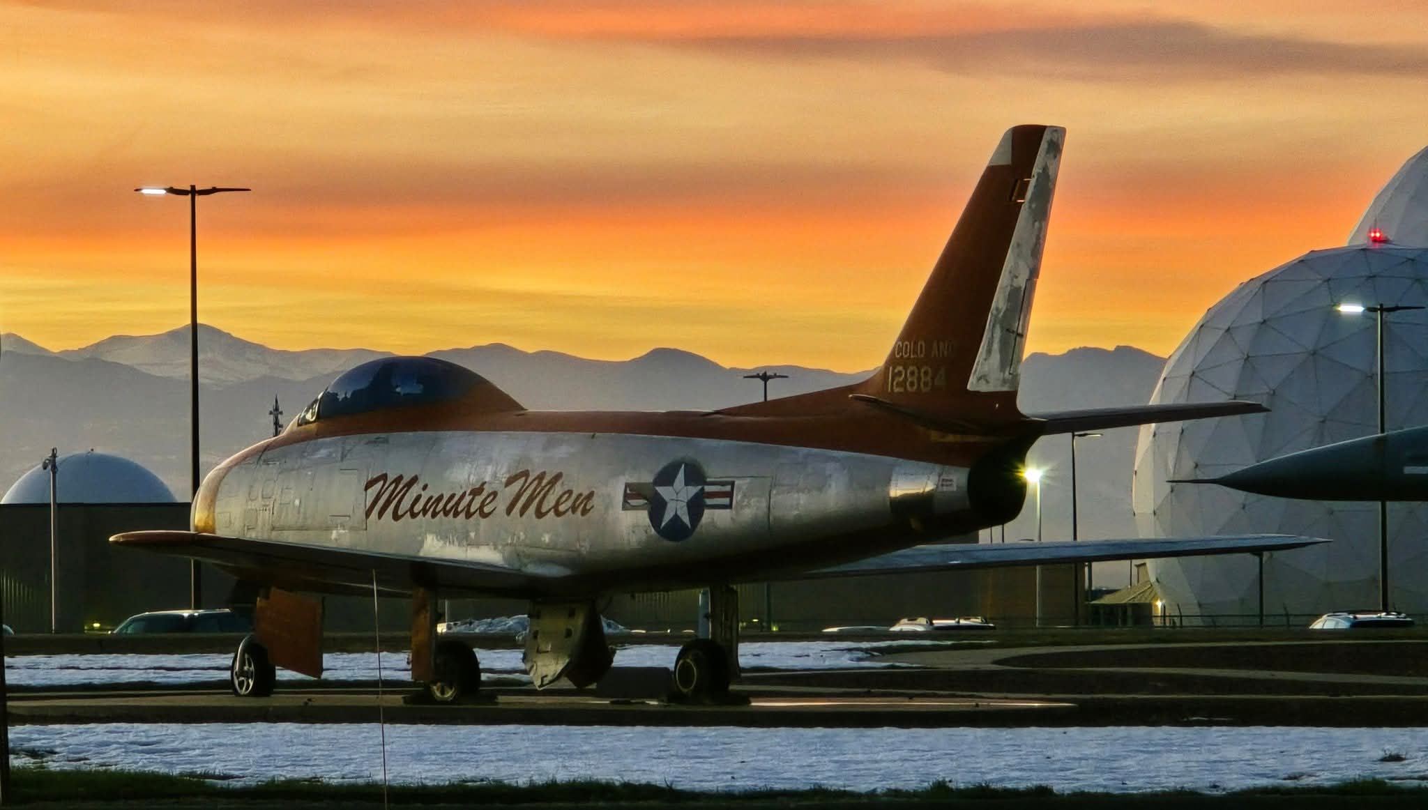 A weathered Cold War-era fighter jet named Minute Men, parked at sunset near radar domes, with mountains in the background.